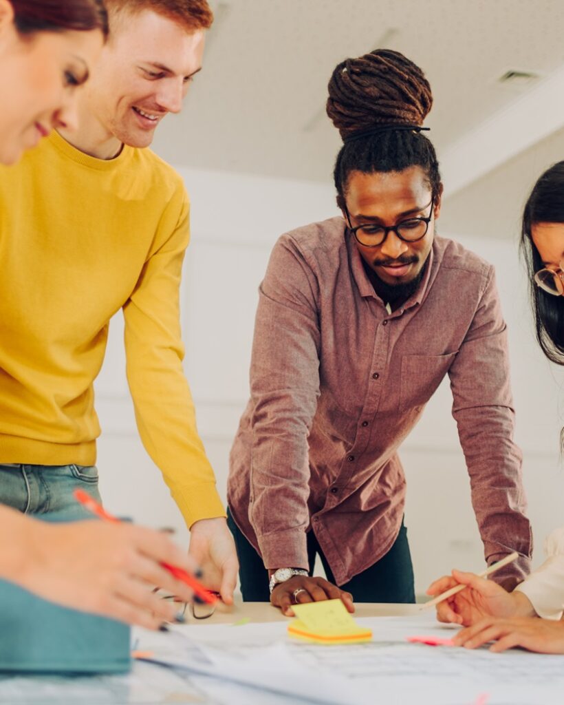 Diverse architect and engineer team discussing about floor plan of building project while having a meeting in an office. Focus on an arabic muslim business man with dreadlocks looking at blueprints.